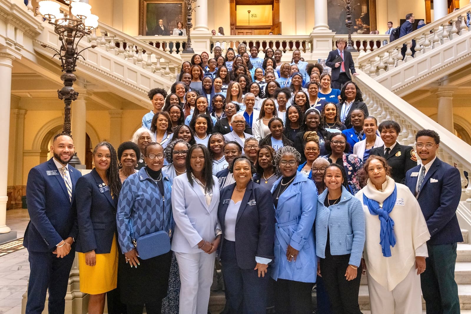 Large group of Black women in blue and white professional attire on a grand staircase.